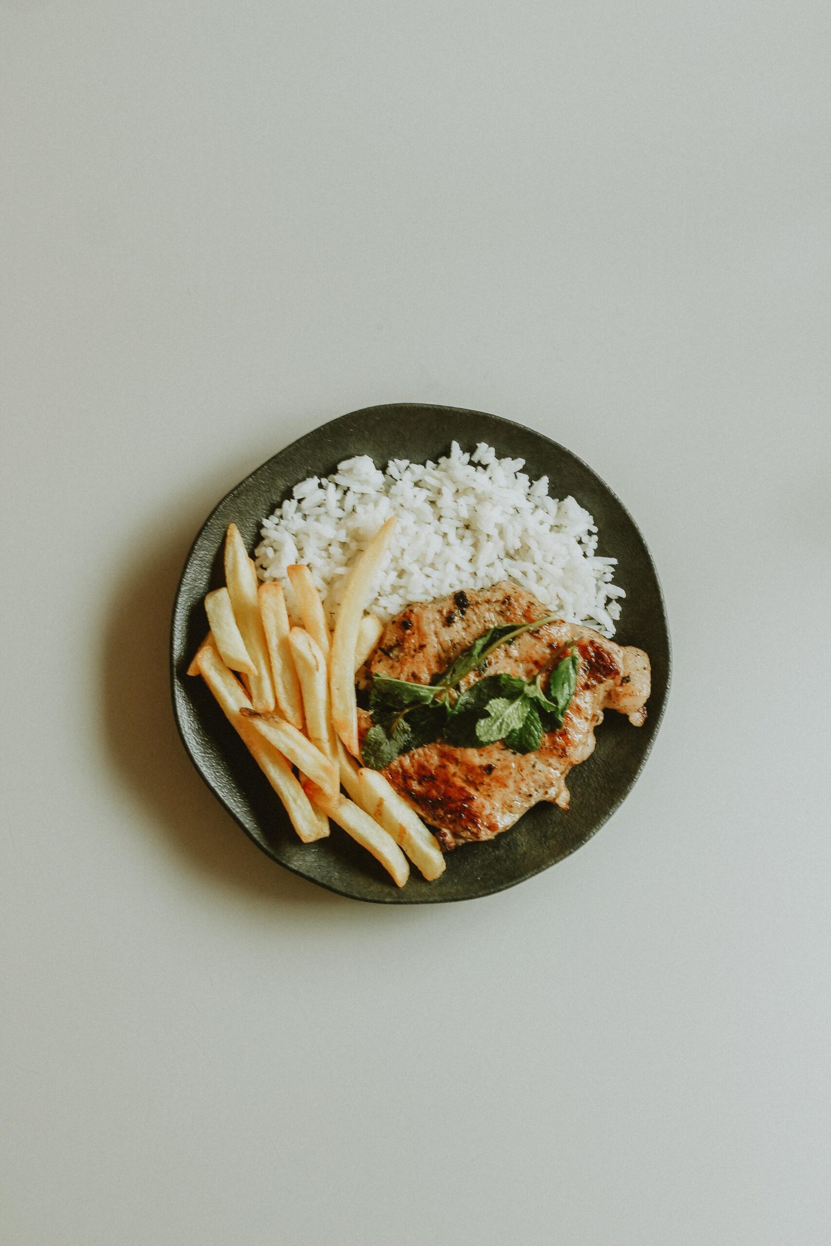 Delicious chicken meal served with fries and rice on a ceramic plate.